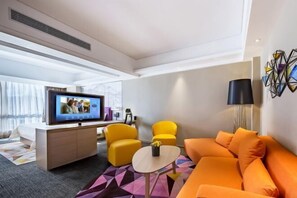 A modern hotel room with a flat-screen TV, yellow armchairs, an orange sofa, a small round table, and a geometric wall decoration. - Hampton by Hilton Lijiang Old Town (Lijiang)