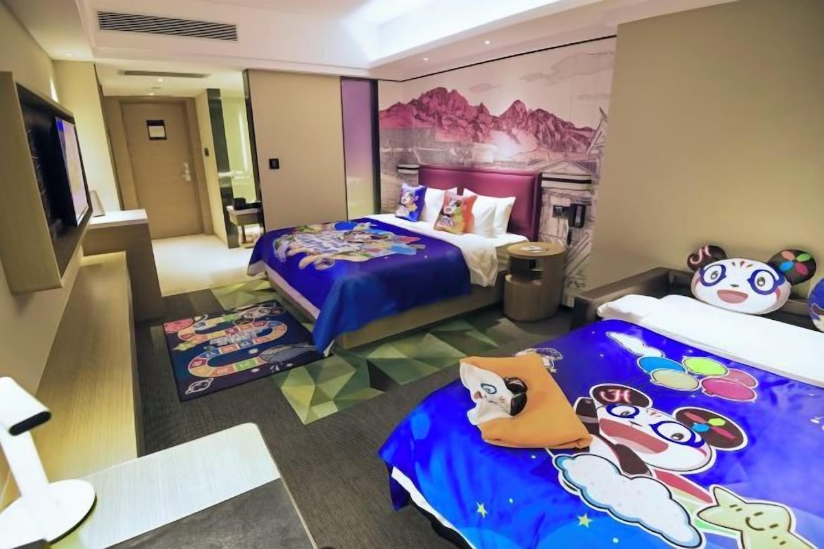 A hotel room with a bed, a desk, a chair, a nightstand, and a wall with a mountain painting.