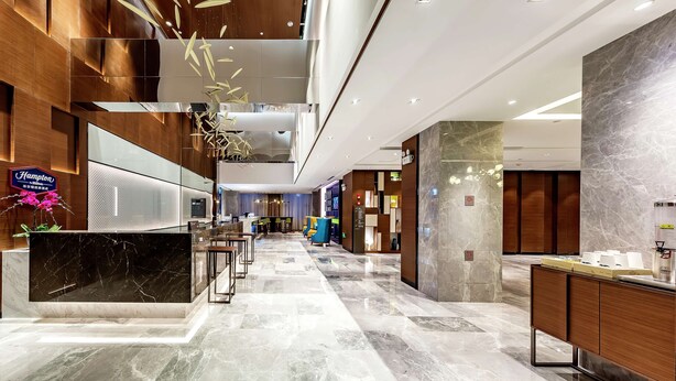 Eine moderne Hotelhalle mit einer Marmor-Rezeption, Holzakzenten und einer hohen Decke mit eingelassener Beleuchtung.