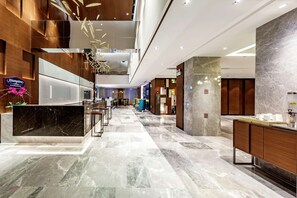 Un moderno vestíbulo de hotel con un mostrador de recepción de mármol, detalles de madera y un techo alto con iluminación empotrada.