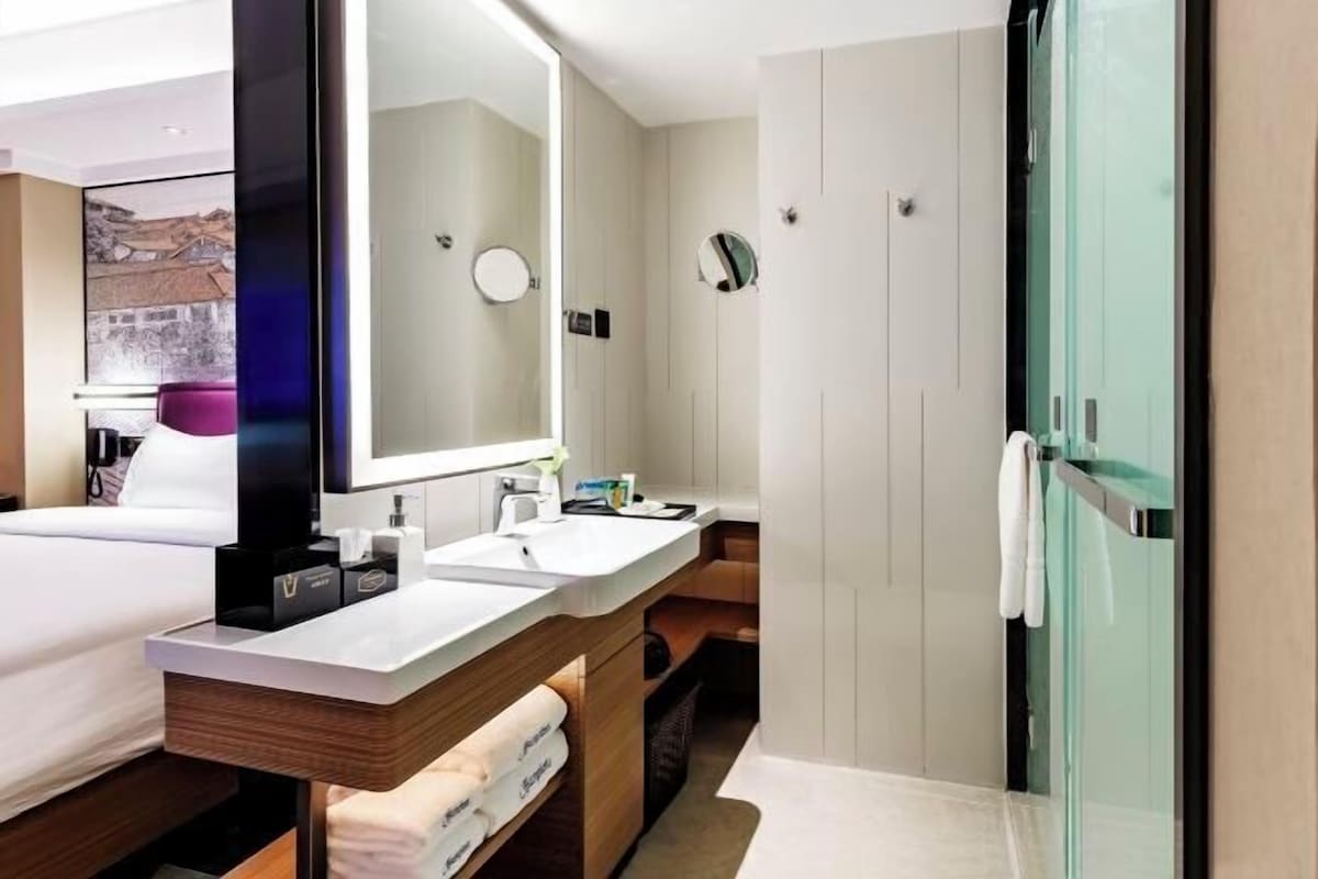 A modern hotel bathroom with a large mirror, two sinks, a shower, and a glass-enclosed shower area.
