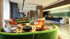 Un lobby moderno con un mostrador de recepción, asientos verdes y naranja, y un suelo con estampado geométrico.