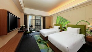 Habitación de hotel con dos camas, un escritorio, una silla, un televisor y un ventanal con vistas a edificios altos.