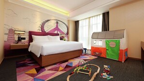 Una habitación de hotel con una cama, un tren de juguete y una zona de juegos.
