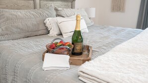 A neatly made bed with a wooden headboard, a wooden tray with a bottle of wine, a glass, and a bowl of strawberries. - The Sunset Ranchette : Luxury Paso Robles Getaway! (Paso Robles)