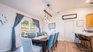 A dining area with a wooden table, blue chairs, and a kitchen area with wooden cabinets and a white countertop. - The Sunset Ranchette : Luxury Paso Robles Getaway! (Paso Robles)