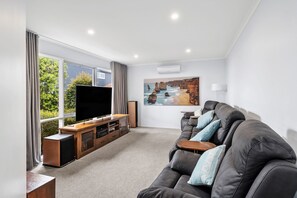 A modern living room with a large flat-screen TV, a leather sofa, and a painting of a coastal landscape.