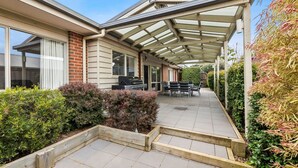 Ein überdachter Patio-Bereich mit Gartenmöbeln, einem Grill und Blick auf das Haus.