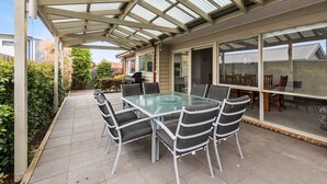 Eine überdachte Terrasse mit Glastisch und Stühlen, einem Grill und Blick auf die Nachbarschaft.