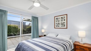 Ein Schlafzimmer mit einem Bett, zwei Nachttischen, einem Deckenventilator, einem gerahmten Kunstwerk und einer Glastür, die zu einem Balkon führt.