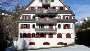 A multi-story building with a symmetrical facade, balconies, and red shutters. - Appartement Odyssée - Welkeys (Megève)