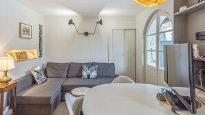 A modern living room with a grey sofa, a white coffee table, a TV, and a lamp. - Appartement Odyssée - Welkeys (Megève)