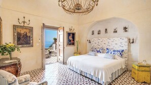 A bedroom with a large bed, a chandelier, and a view of the sea through an open door. - Villa San Giacomo - Unique Villa in Positano (Positano)