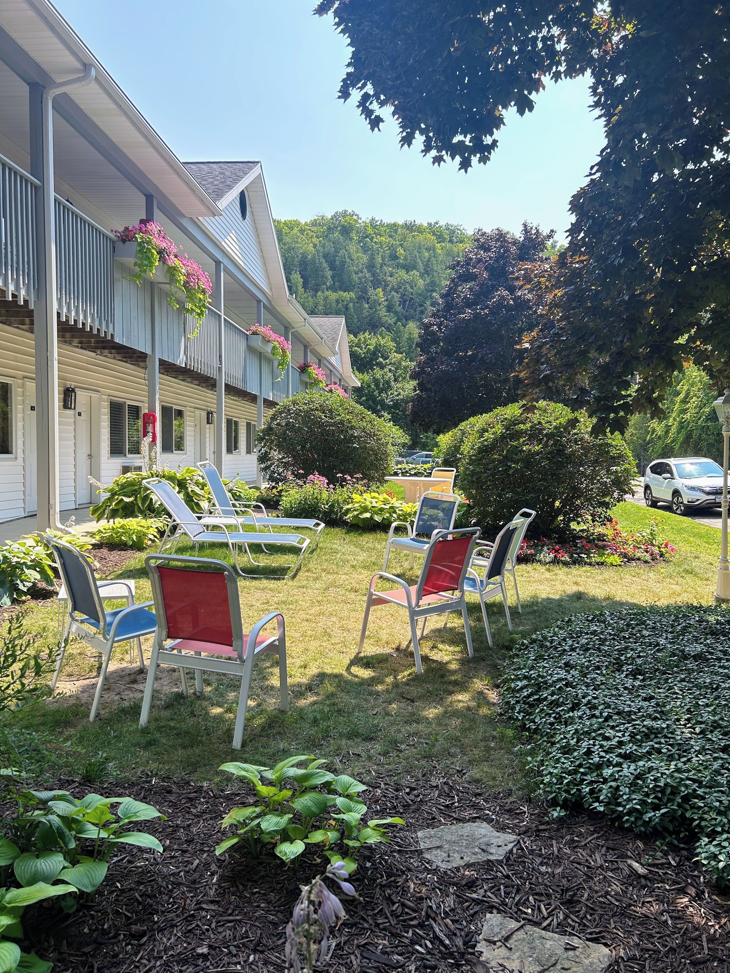 A hotel with a covered outdoor seating area, surrounded by well-maintained gardens and a variety of plants.