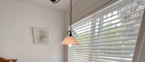 A hotel room with a bed, a wooden table, two chairs, a hanging lamp, and a window with blinds.