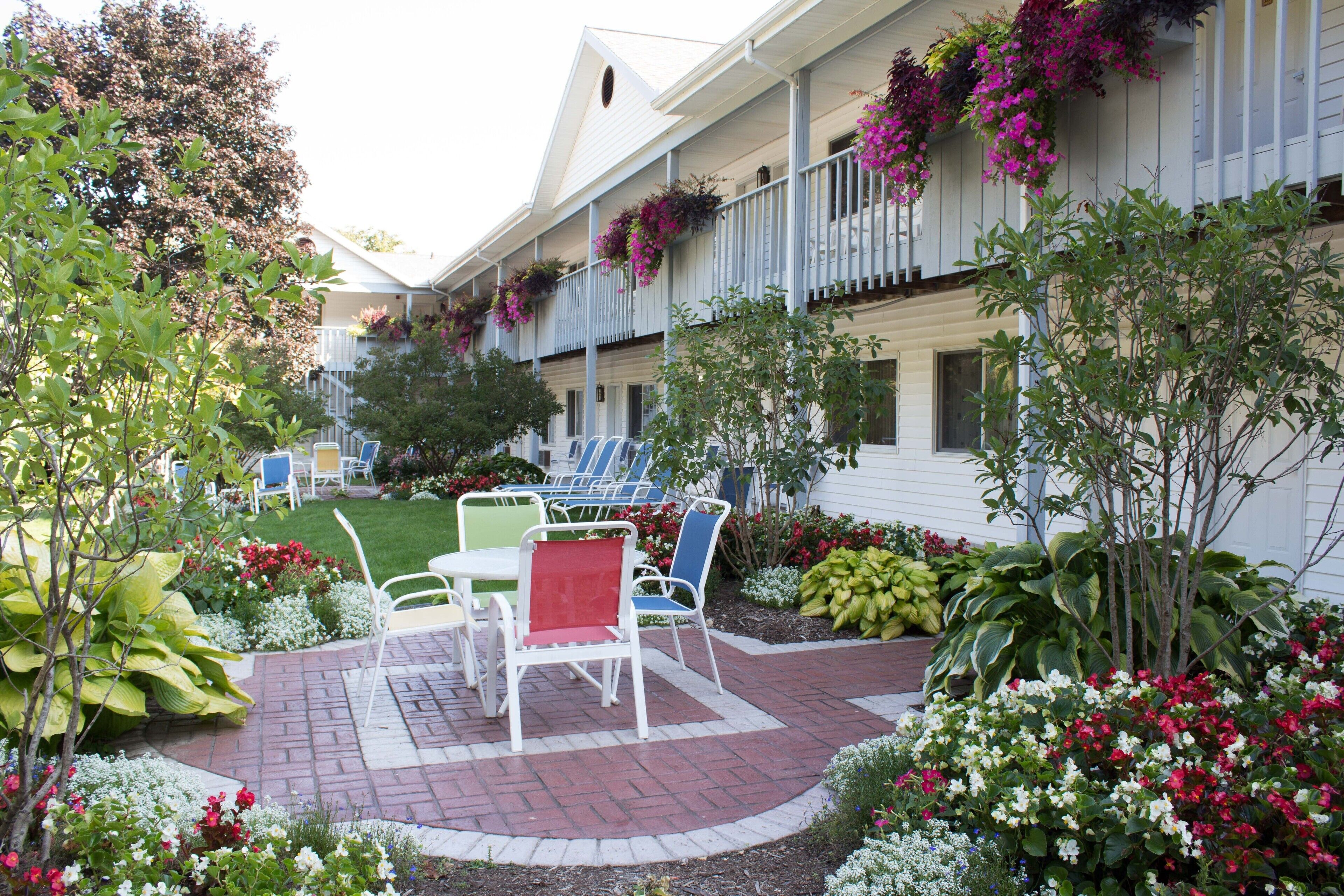 A hotel courtyard with outdoor seating, a brick patio, and a variety of plants and flowers.