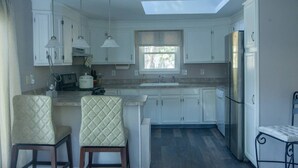 Une cuisine moderne avec des armoires blanches, un puits de lumière, un réfrigérateur et deux chaises.
