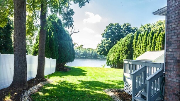 Un jardin avec une clôture blanche, une terrasse et une vue sur un lac.