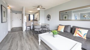 Un salon moderne avec un canapé gris, une table basse blanche et un coin repas comprenant une table et des chaises grises.