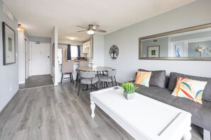 A modern living room with a gray sofa, a white coffee table, and a dining area with a gray table and chairs.