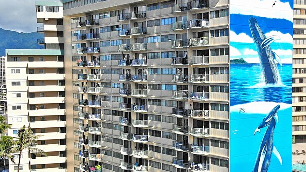 Un hôtel de grande hauteur doté de nombreux balcons, d’un espace piscine et d’une grande fresque représentant des baleines sur l’un de ses murs.