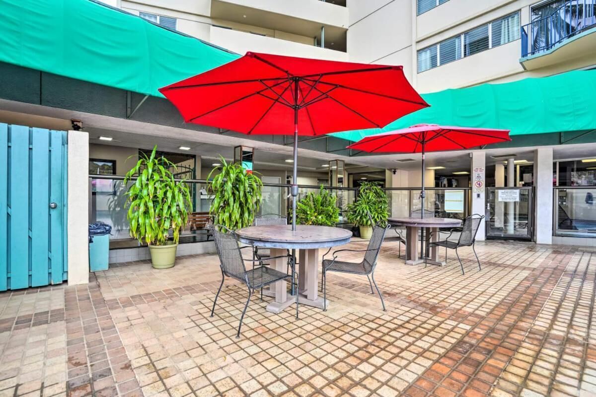 An outdoor patio area with round tables and chairs, red umbrellas, and potted plants.