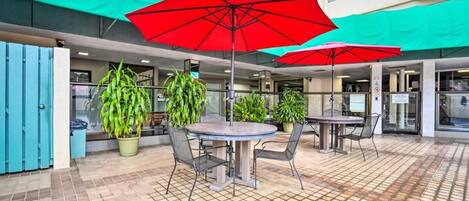 An outdoor patio area with round tables and chairs, red umbrellas, and potted plants.