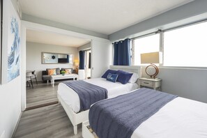 A hotel room with two beds, a desk, a chair, a mirror, and a window with curtains.