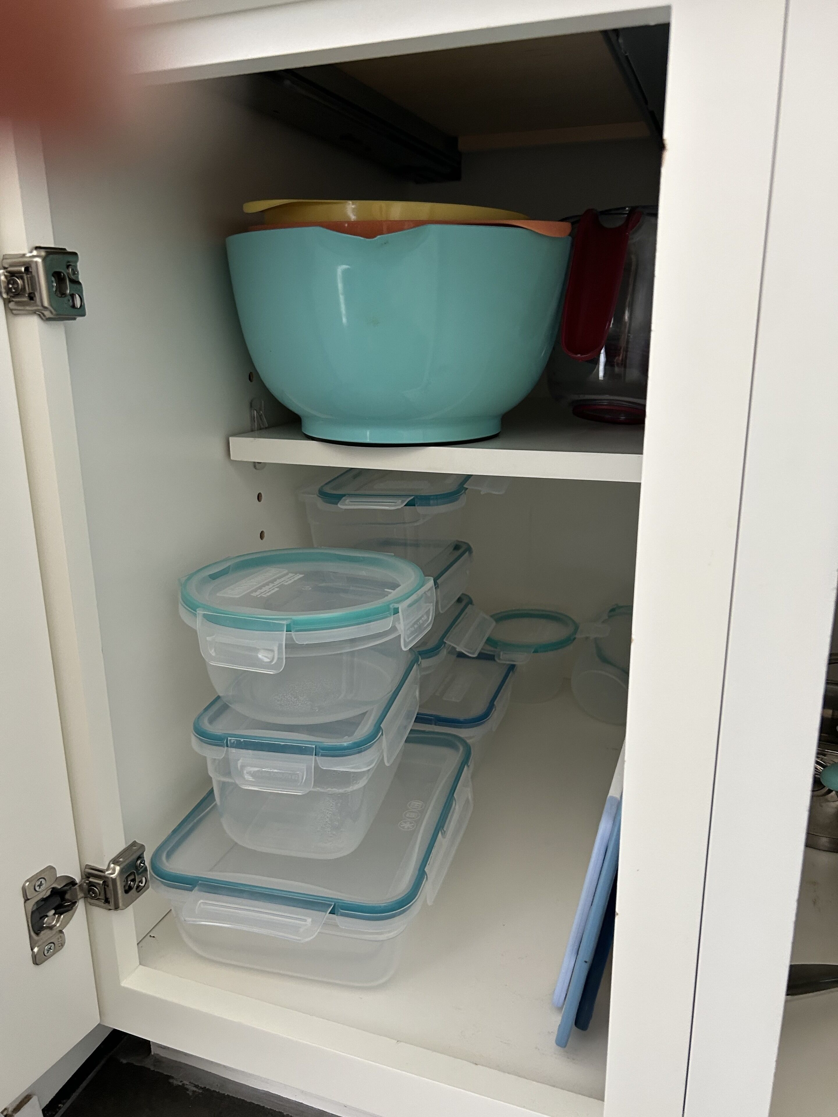 A kitchen cabinet with a teal bowl on the top shelf and clear plastic storage containers on the bottom shelf.