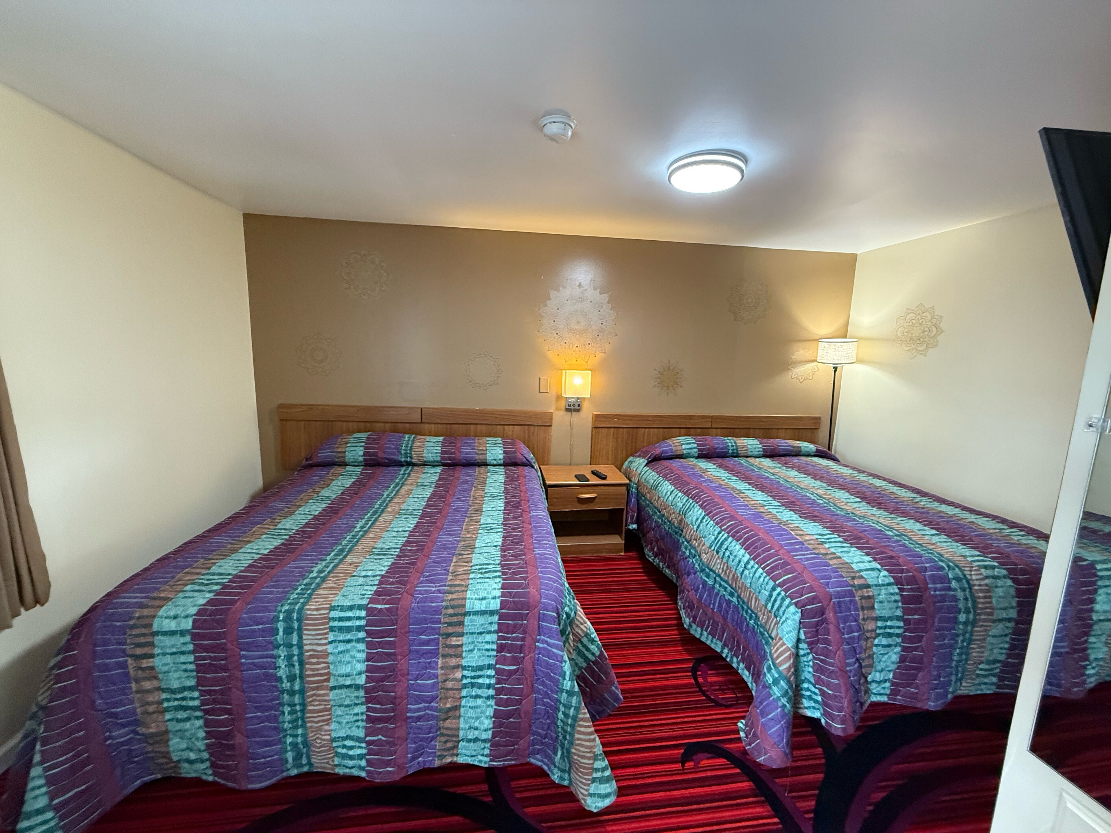 Camera d'albergo con due letti, ognuno con copripiumino a righe, un comodino, una lampada e una luce a soffitto.