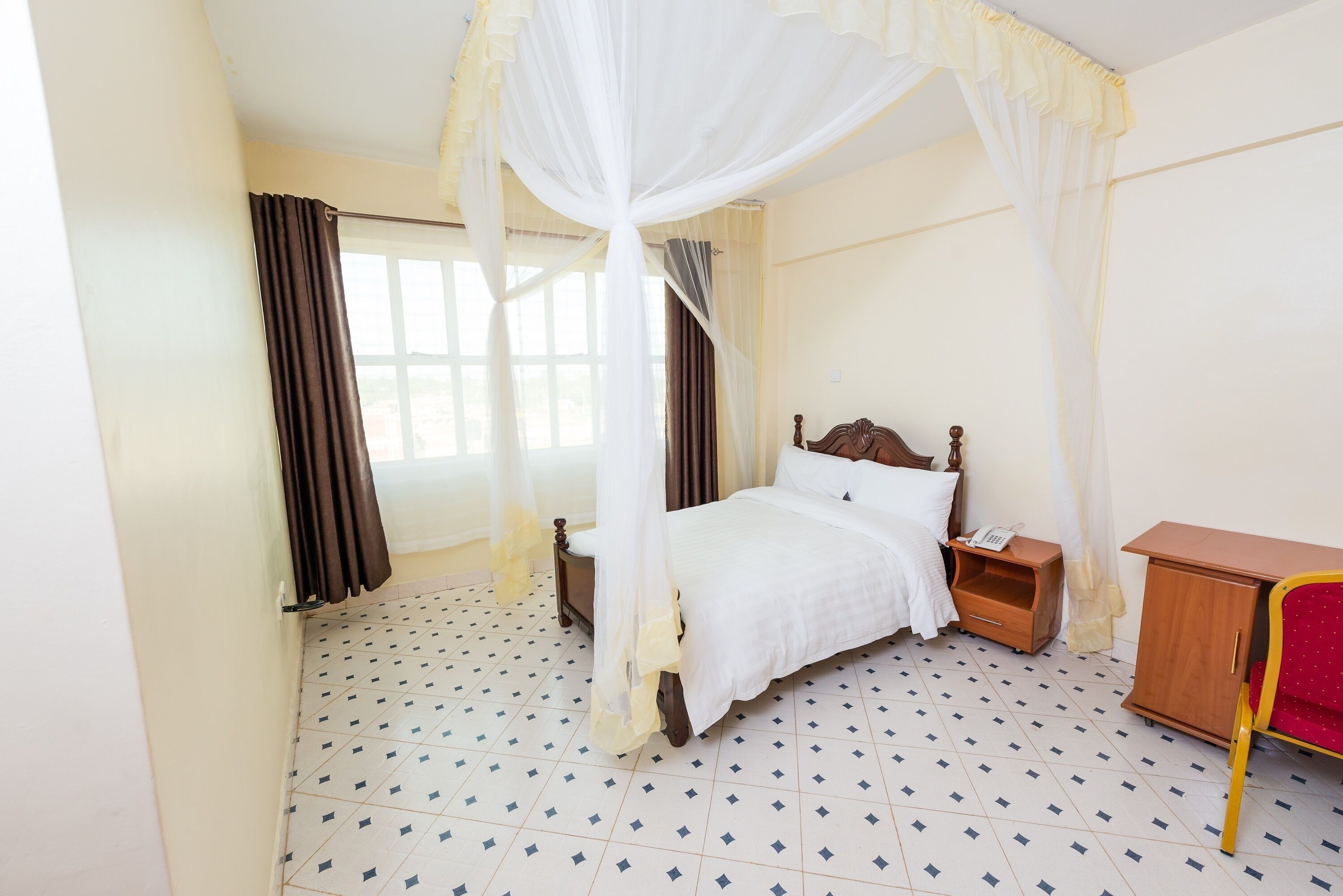 A bedroom with a four-poster bed, a wooden nightstand, a wooden cabinet, and a red chair.