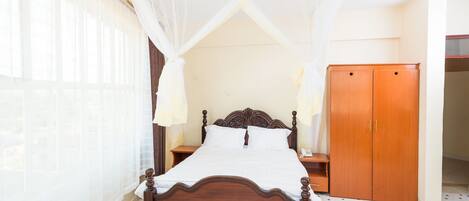 A bedroom with a wooden bed, a nightstand, a wardrobe, and a window with sheer curtains.