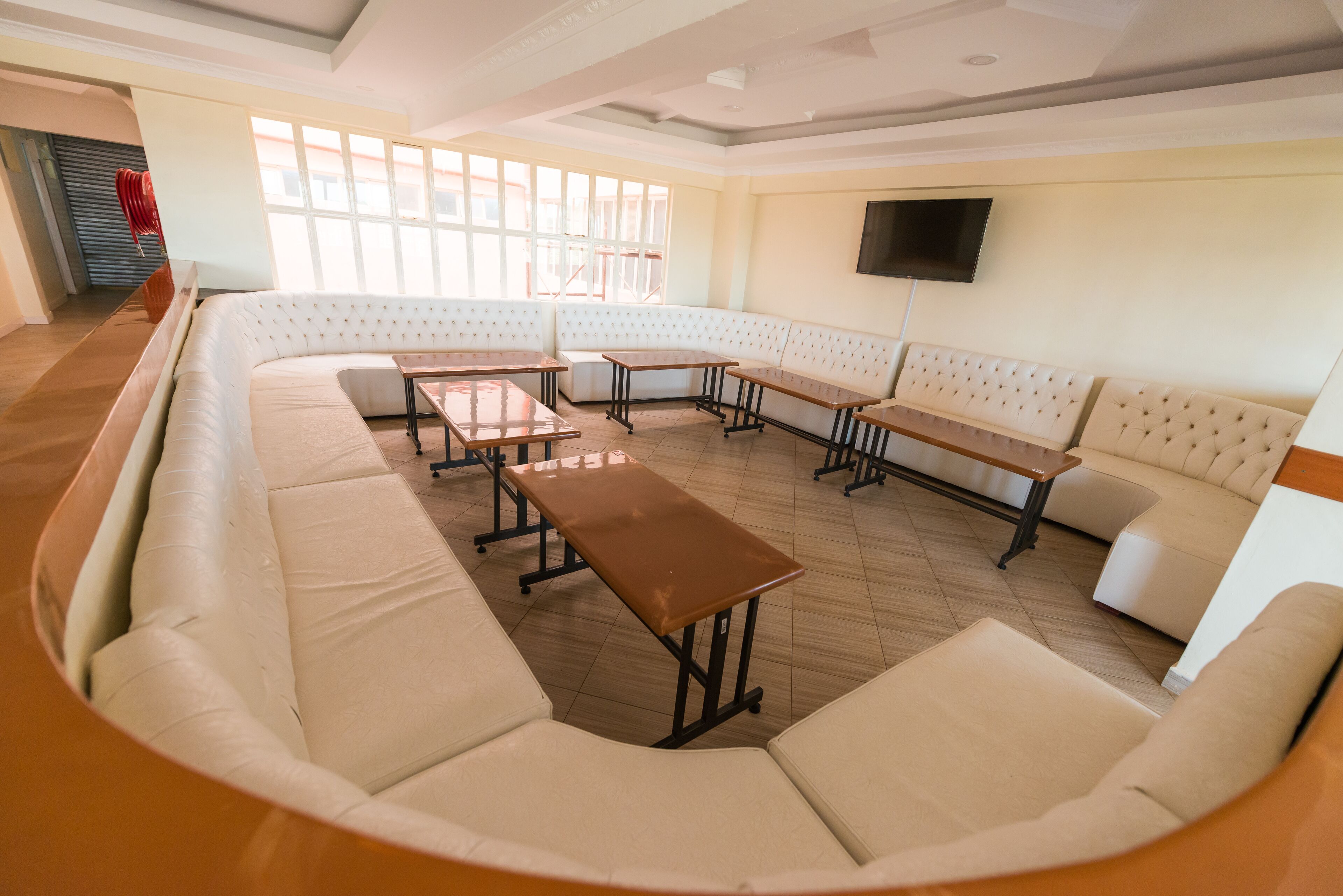 A spacious room with a curved sofa, multiple tables, and a television mounted on the wall.