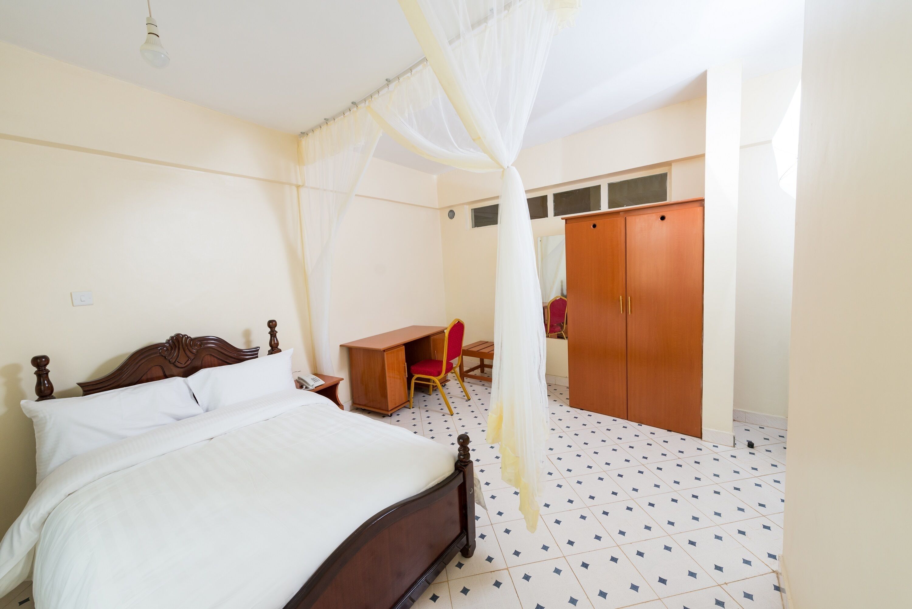 A bedroom with a bed, a desk, a chair, a wardrobe, and a mosquito net.