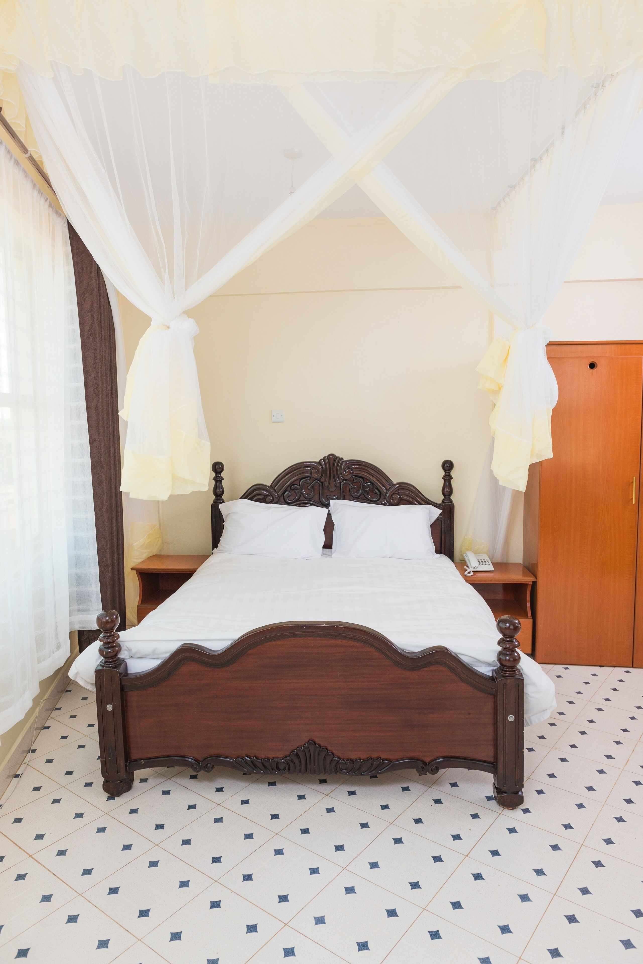 A bed with a wooden frame and white bedding, a wooden nightstand with a telephone, and a wardrobe.
