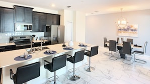 A modern kitchen with dark cabinets, stainless steel appliances, and a bar area with bar stools. - Ocean Breeze by Florida Spirit (Kissimmee)