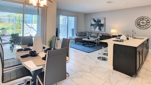 A modern living room with a dining area, a kitchen, and a large window overlooking a garden. - Ocean Breeze by Florida Spirit (Kissimmee)