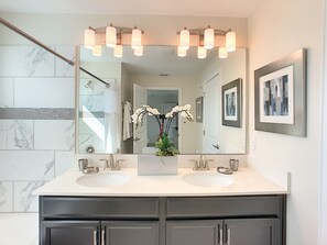 A bathroom with a large mirror, two sinks, and a vase with orchids.