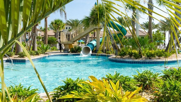 A pool area with a water slide, palm trees, and a clear blue pool. - Ocean Breeze by Florida Spirit (Kissimmee)