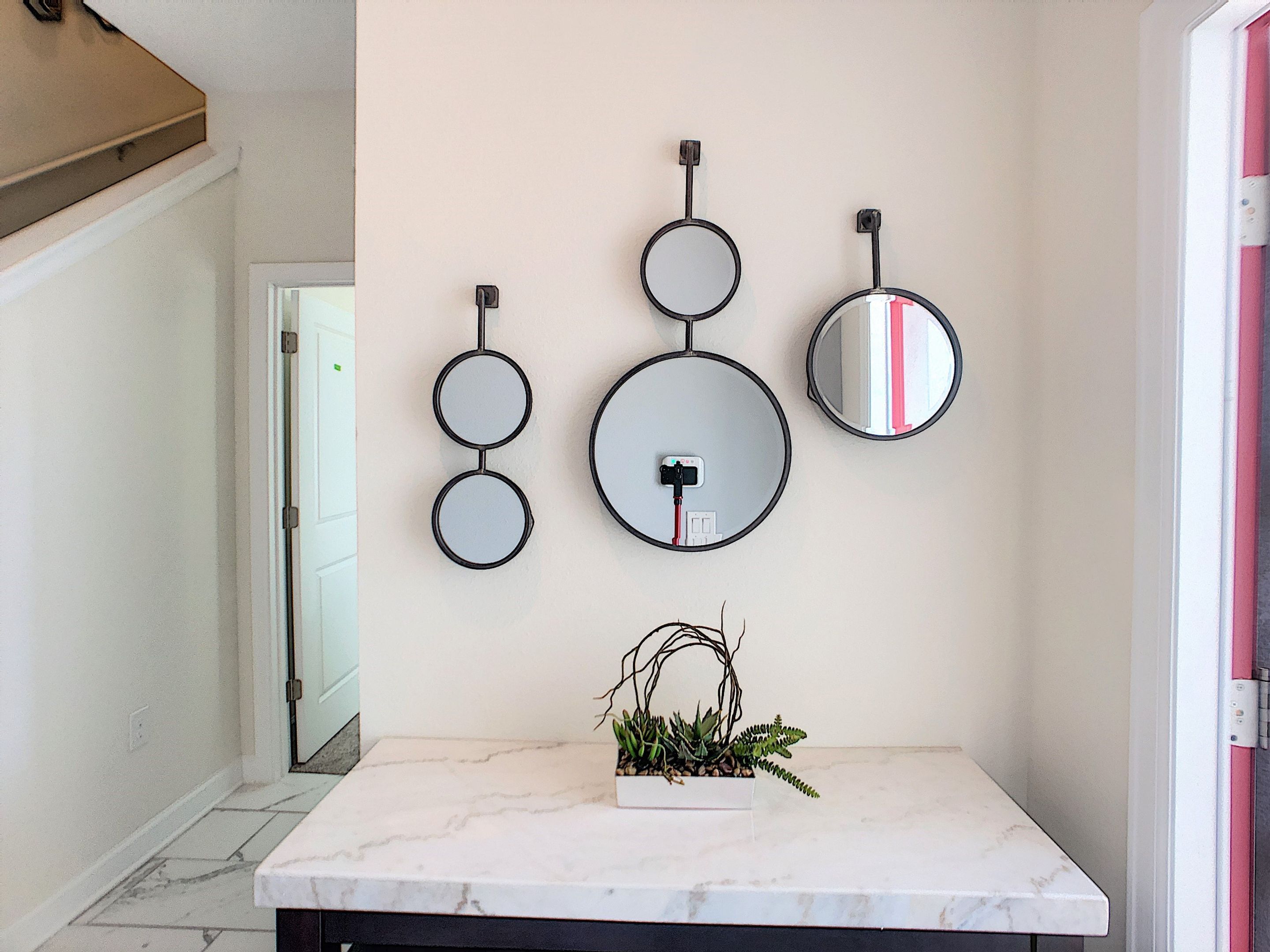 A hallway with a marble-topped table, a potted plant, and three wall-mounted mirrors of varying sizes.