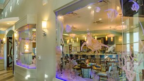 A hotel lobby with a large aquarium window, a reception desk, and a bar area. - Ocean Breeze by Florida Spirit (Kissimmee)