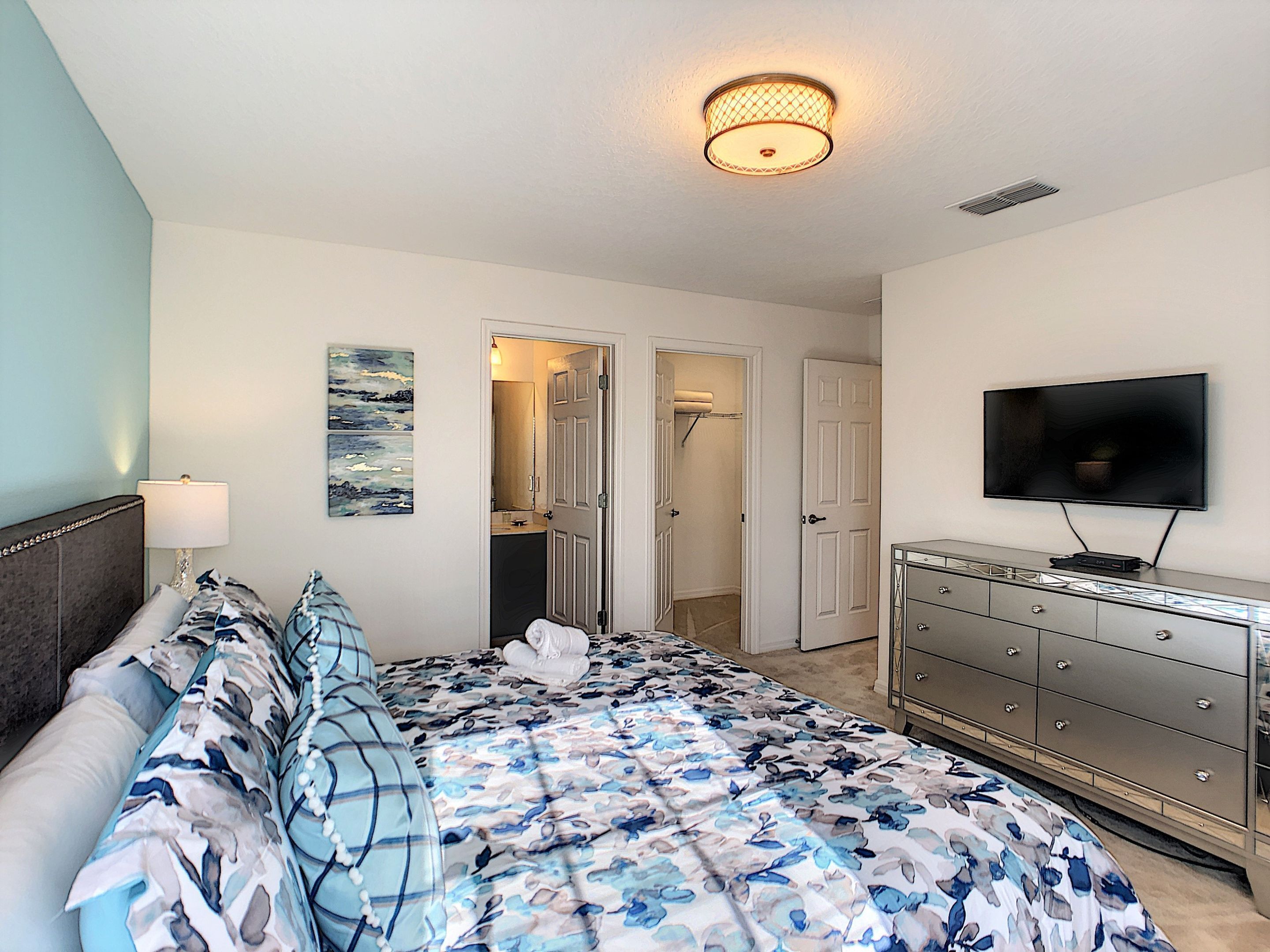 A bedroom with a bed, dresser, television, and artwork on the wall.