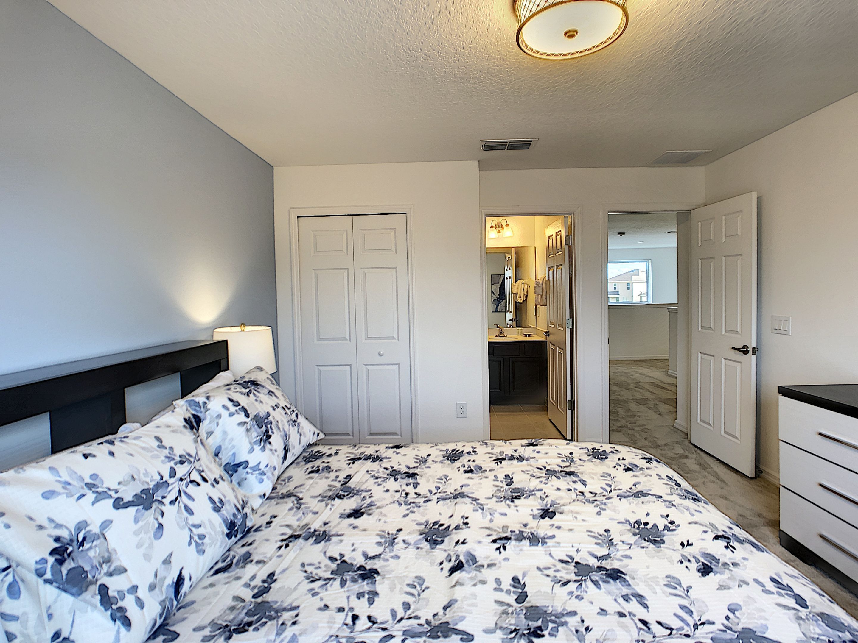 A bedroom with a bed, a nightstand, a dresser, and a bathroom visible through an open door.