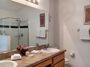 A bathroom with a large mirror, two sinks, a shower, and a toilet.