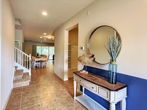 A hallway with a staircase, a dining area, and a vanity with a mirror and decorative items.