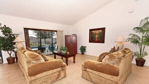 Ein Wohnzimmer mit zwei Sofas, einem Couchtisch und einem Schrank. Ein Fenster bietet Blick auf einen Pool, und eine Tür führt nach draußen.