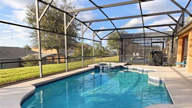 Ein Swimmingpool mit Glasveranda, umgeben von einer Terrasse und Blick auf eine Wohngegend.