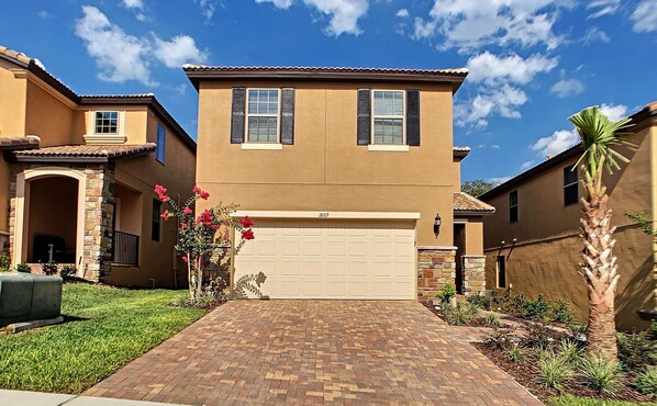 A two-story house with a garage, a brick driveway, and a well-maintained lawn.