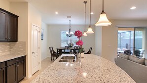 A kitchen with granite countertops, dark wooden cabinets, a central island, and pendant lighting. - Dahlia Garden by Florida Spirit (Kissimmee)