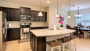 A modern kitchen with dark cabinetry, stainless steel appliances, and a central island with bar stools. - Dahlia Garden by Florida Spirit (Kissimmee)